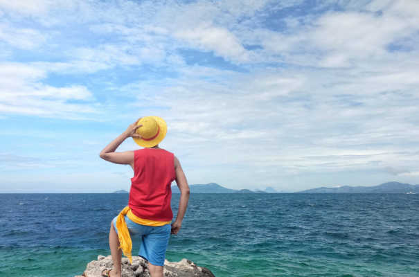 Persona su scogliera, mare vasto, cielo aperto, avventura e libertà.